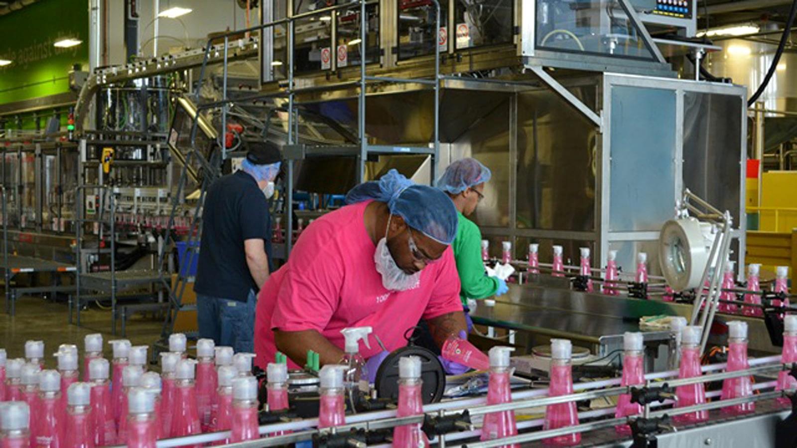 Opératrice avec filet à cheveux sur une chaîne de production de bouteilles roses