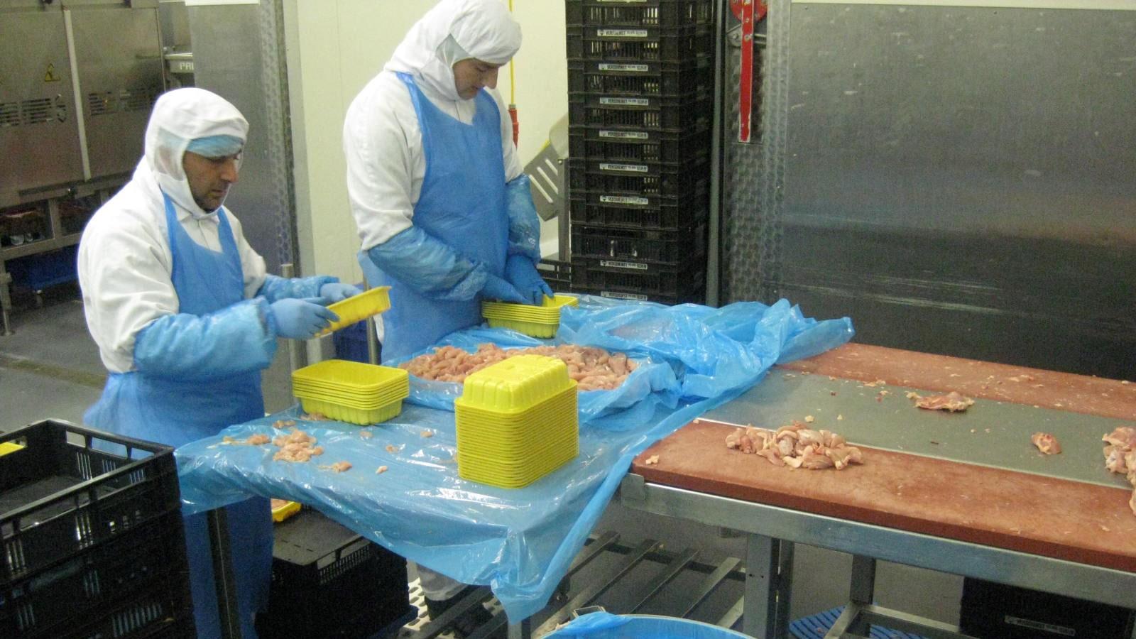 Deux employés chez Scheria conditionnent du poulet dans des sacs plastiques