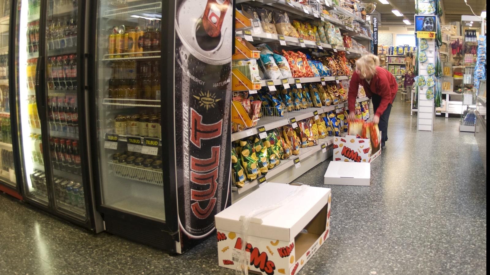 Une jeune employée remplit les rayons de chips dans un magasin SuperBrugsen